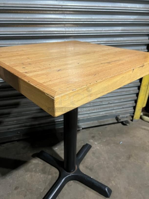 Commercial dining-height table with a solid wood top and black metal pedestal base. Light wear visible on surface.