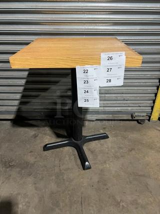 Commercial dining-height table with light wood top and metal pedestal base. Tags indicate quantities and auction lot numbers.