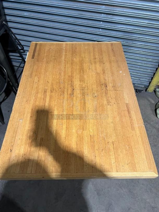 Commercial wooden rectangular tabletop with pedestal base, showing wear and natural wood grain, in used condition.
