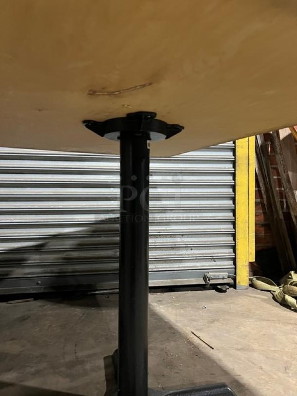 Commercial wooden rectangular tabletop with a black pedestal base, showing minor wear. Ideal for restaurants or cafes.