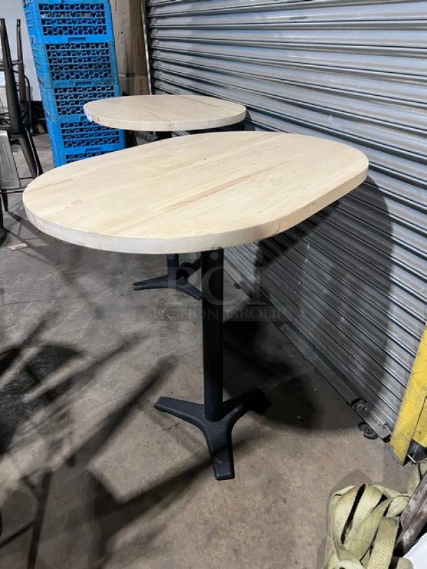 Commercial wooden oval tabletop with pedestal base, light wood finish, sturdy black metal support, excellent condition.