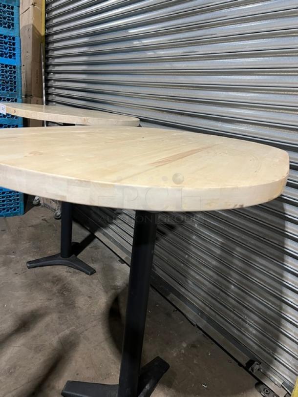 Oval wooden tabletop with pedestal base, commercial-grade, light finish, good condition, ideal for restaurants or cafes.