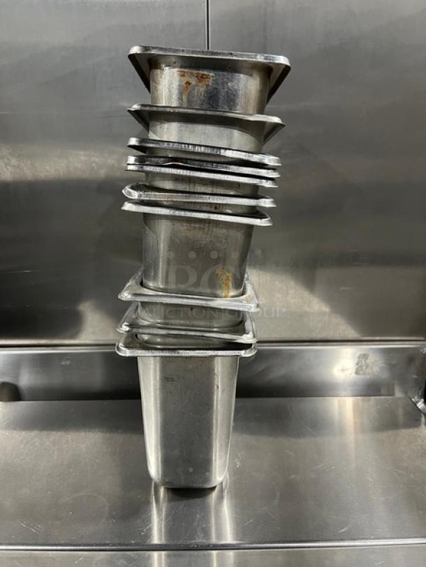 Stack of commercial stainless steel hotel/steamtable pans, used condition, various sizes, key for food service setups.