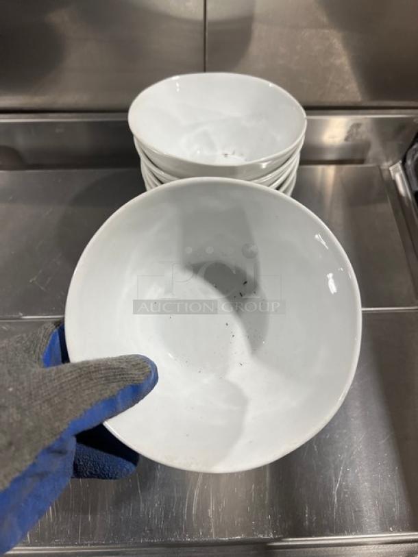 Crate&Barrel white round bowl, commercial grade, lightly soiled, held by gloved hand. Set of bowls stacked behind.