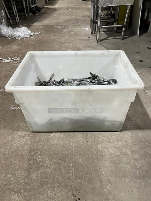 Plastic bin filled with assorted commercial stainless steel dining utensils, including forks, knives, and spoons.