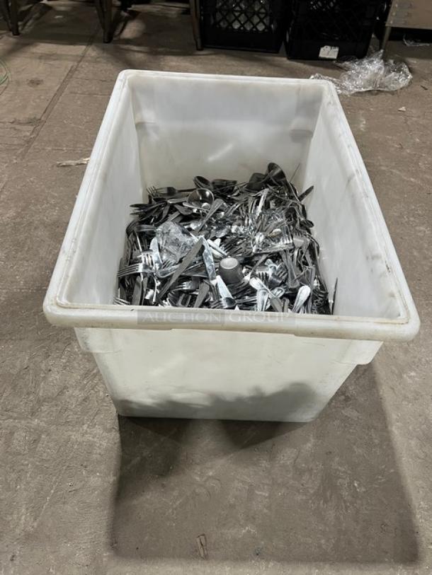 Commercial stainless steel dining utensils in a large white bin, including forks, knives, and spoons. Mixed condition.