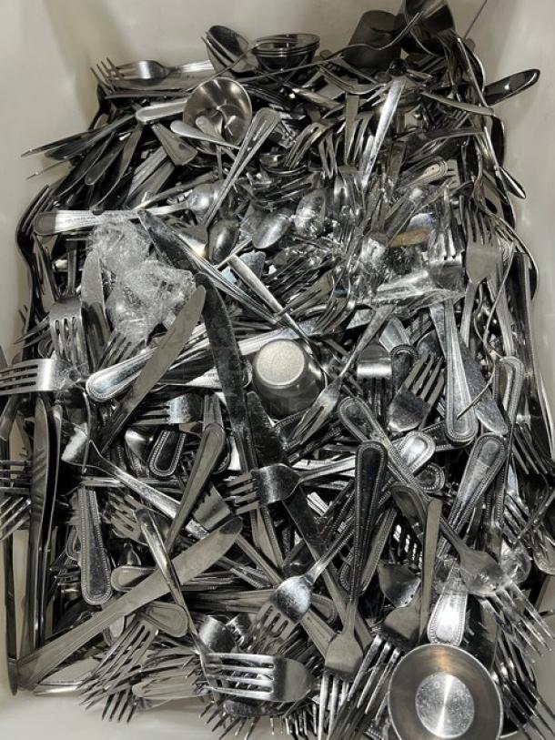 Stainless steel dining utensils assortment, including forks, knives, and spoons. Commercial-grade, shiny, and stacked in bulk.