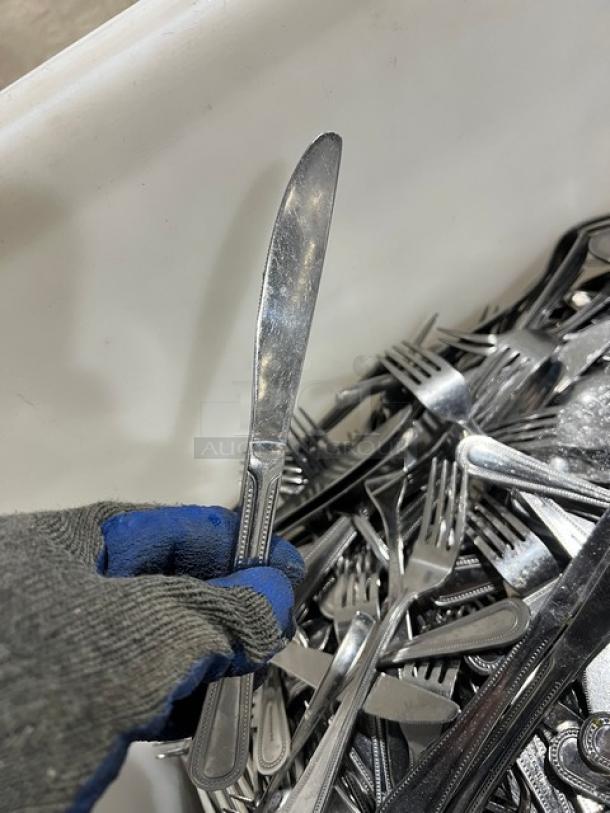 Stainless steel dining utensils, including forks, knives, and spoons, in used condition. Ideal for commercial use.