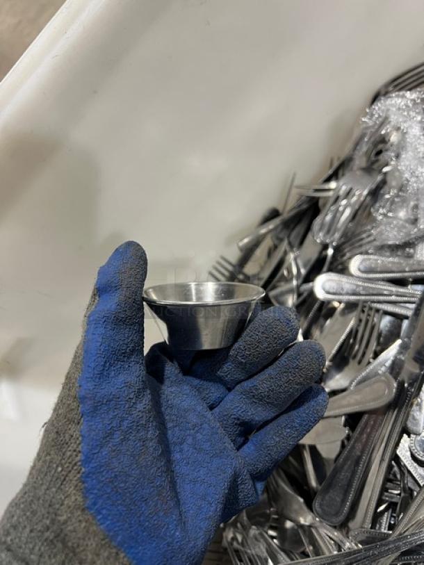 Commercial stainless steel dining utensils including forks, knives, and spoons in a bin. A gloved hand holds one item.