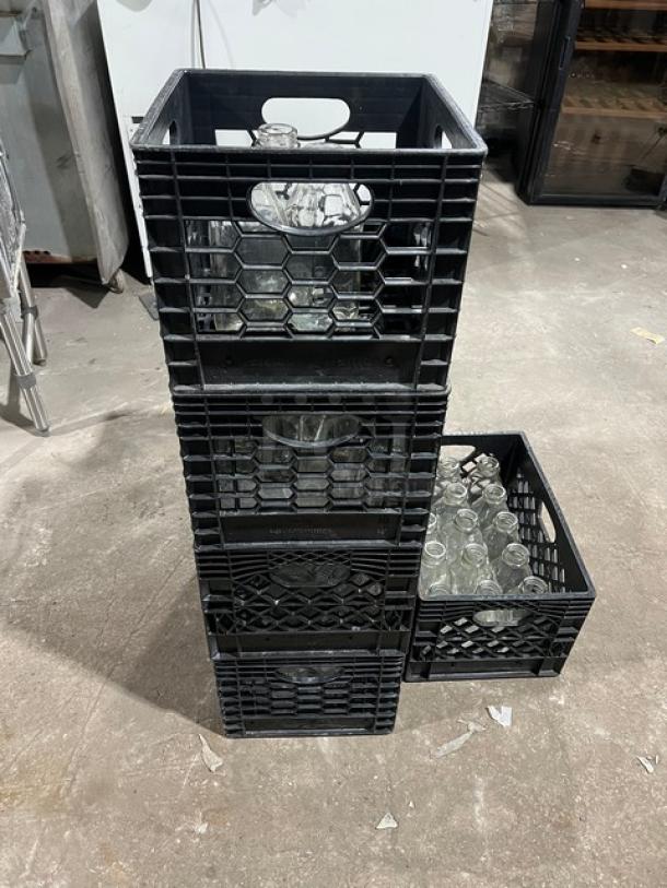 Eight stacked crates of commercial water/juice serving bottles; black plastic crates, clear glass bottles, excellent condition.