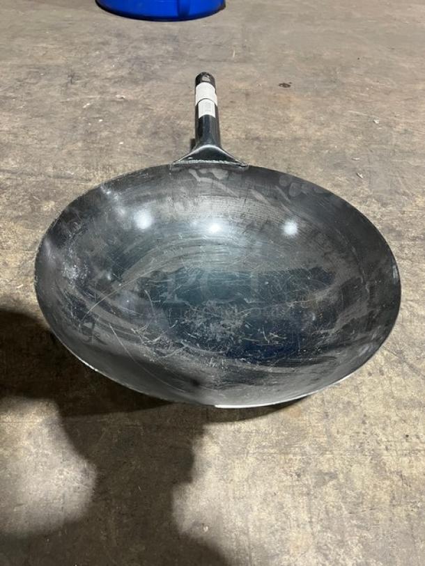 Commercial black non-stick frying pan, scratches visible, metal handle with a label. Used condition, ideal for heavy-duty cooking.