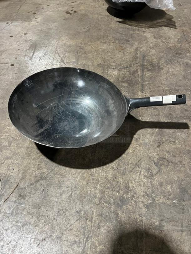 Commercial black non-stick frying pan with long handle; visible scratches; tag on handle; suitable for professional kitchens.