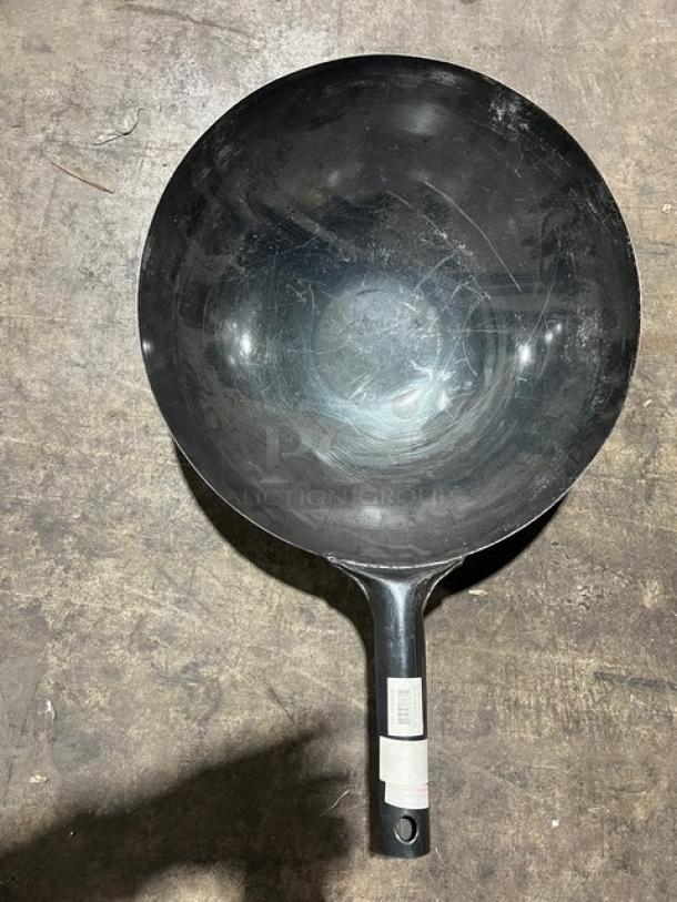 Commercial black non-stick frying pan; used condition with visible wear. Long handle features a label with product info.