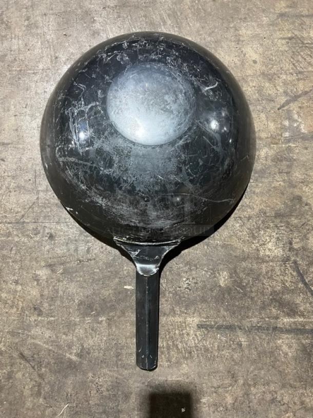 Commercial black non-stick frying pan, round, with a long handle. Shows signs of wear, scratches visible.