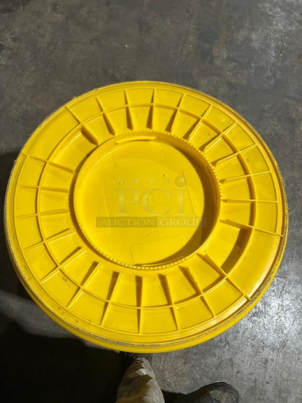 Rubbermaid Brute Series yellow 55-gallon round trash can, lid viewed from above, durable commercial design.