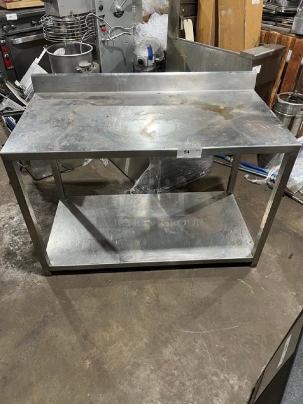Commercial stainless steel food prep work table with undershelf, used, with visible wear and back splash guard.