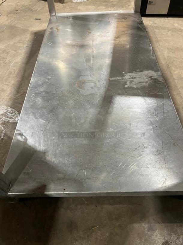 Commercial stainless steel food prep work table with one undershelf, showing signs of use with visible scratches.