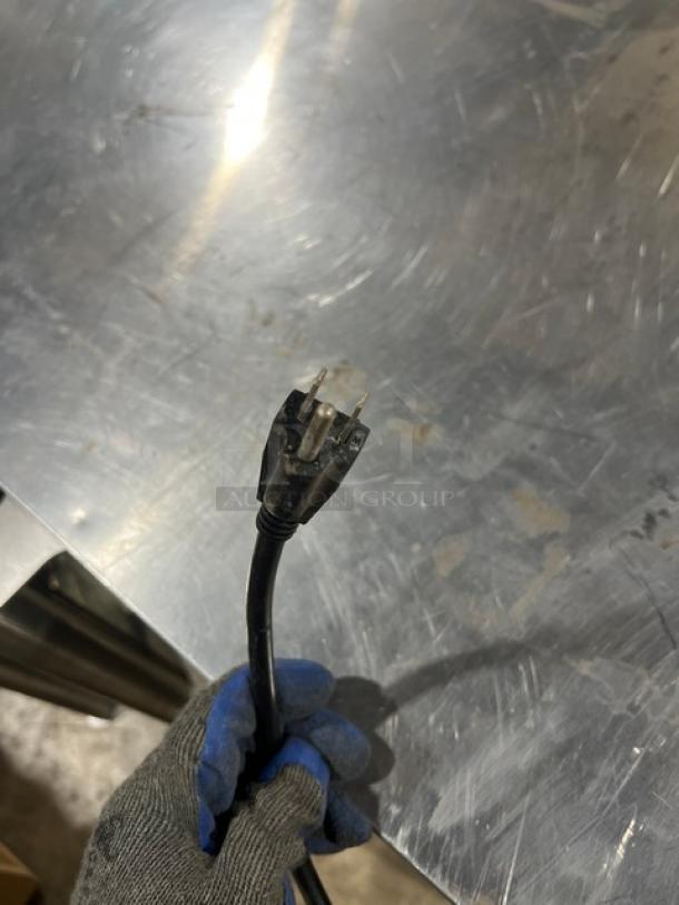 A gloved hand holding a power plug against a stainless steel surface.