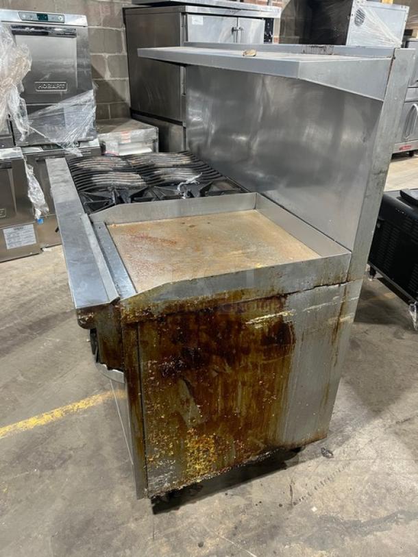 Southbend commercial stainless steel range with griddle, double oven, overhead salamander shelf, back and side splash, on casters. Condition shows visible surface rust and wear.
