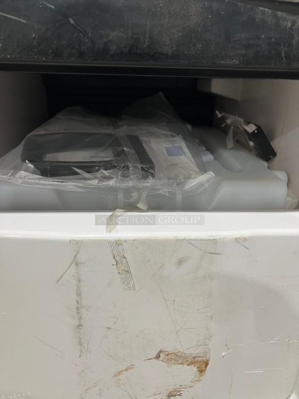 Commercial stainless steel electric ice maker head, scuffed exterior, includes power cord, packaged components visible inside.