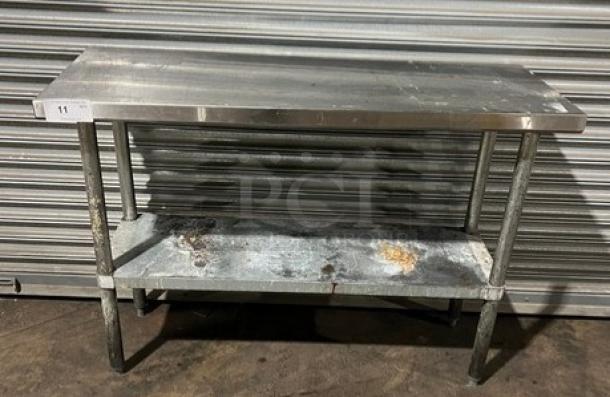 Commercial stainless steel worktop table with single undershelf, on legs. Visible wear and marks indicating use.