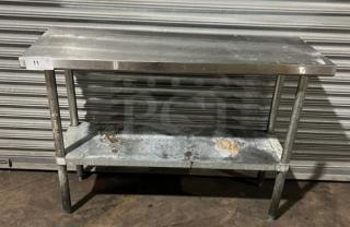 Commercial stainless steel worktop table with single undershelf, on legs. Visible wear and marks indicating use.