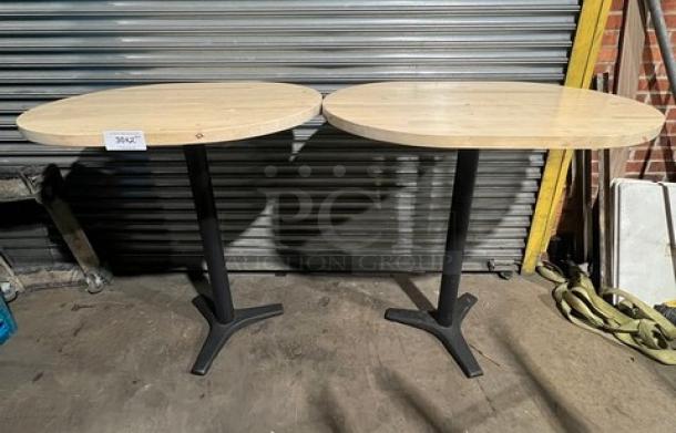 Commercial wooden oval tabletops with pedestal bases, two units shown. Sturdy condition, ideal for dining or business use.