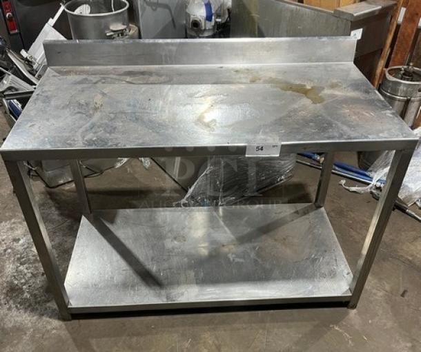 Commercial stainless steel food prep work table with undershelf, used, with visible wear and back splash guard.