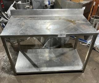 Commercial stainless steel food prep work table with undershelf, used, with visible wear and back splash guard.