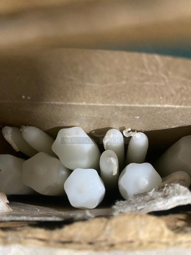 Box of white hand-dipped candles, shown closely, displaying smooth texture and varied sizes, within a cardboard packaging.