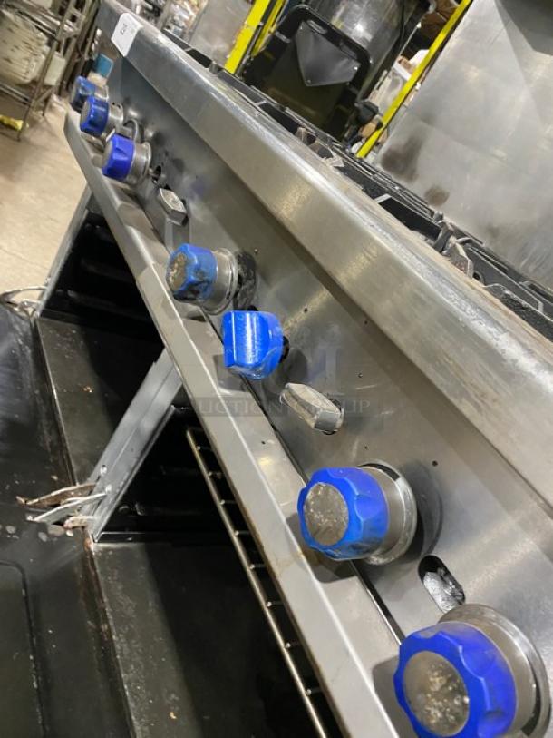 American Range 8-burner gas range with double oven, stainless steel, blue knobs, overhead salamander shelf, on casters.