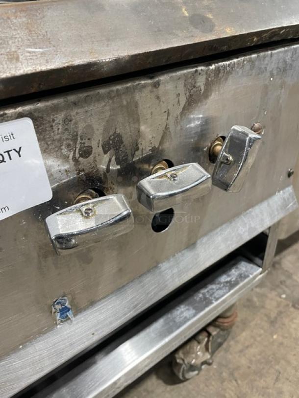 Commercial stainless steel single burner stock pot range, gas powered, on casters. Visible wear; control knobs intact.