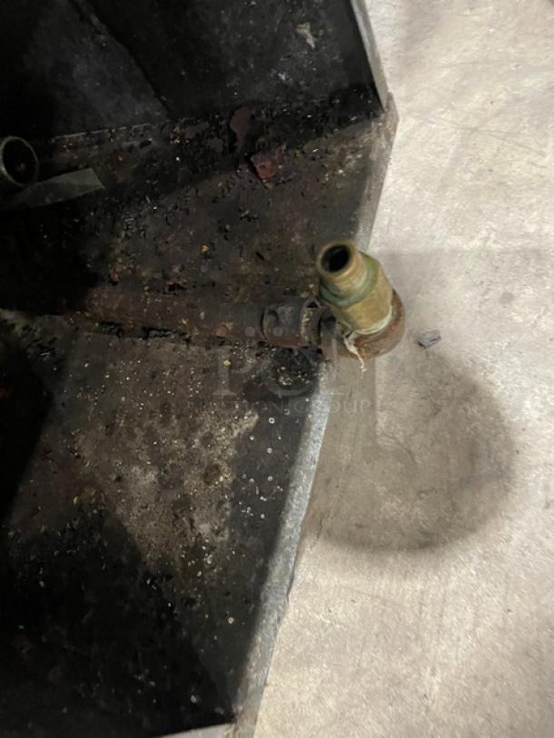 Stainless steel DCS gas-powered deep fryer base with visible dirt and wear, showing a brass connection fitting.