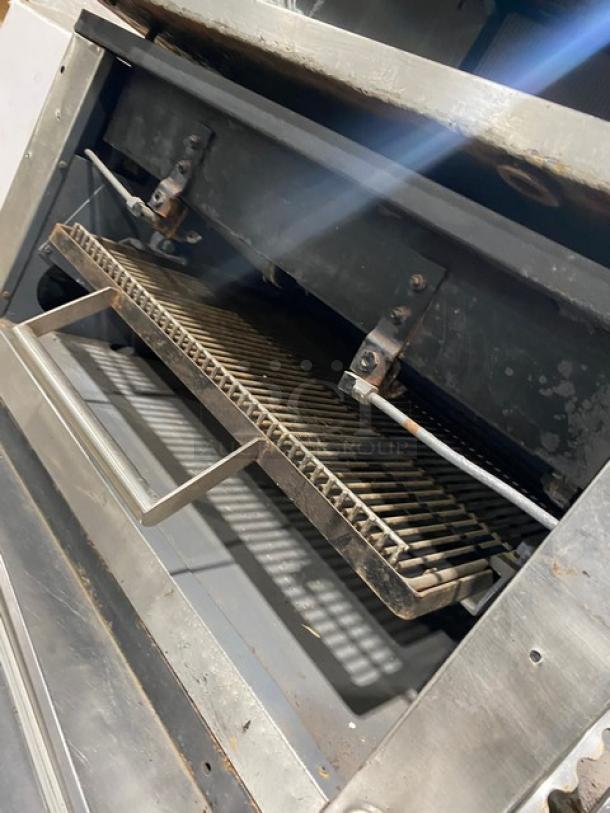 Commercial stainless steel gas countertop flat-griddle with back and side splash, built-in broiler/cheese melter, visible wear.