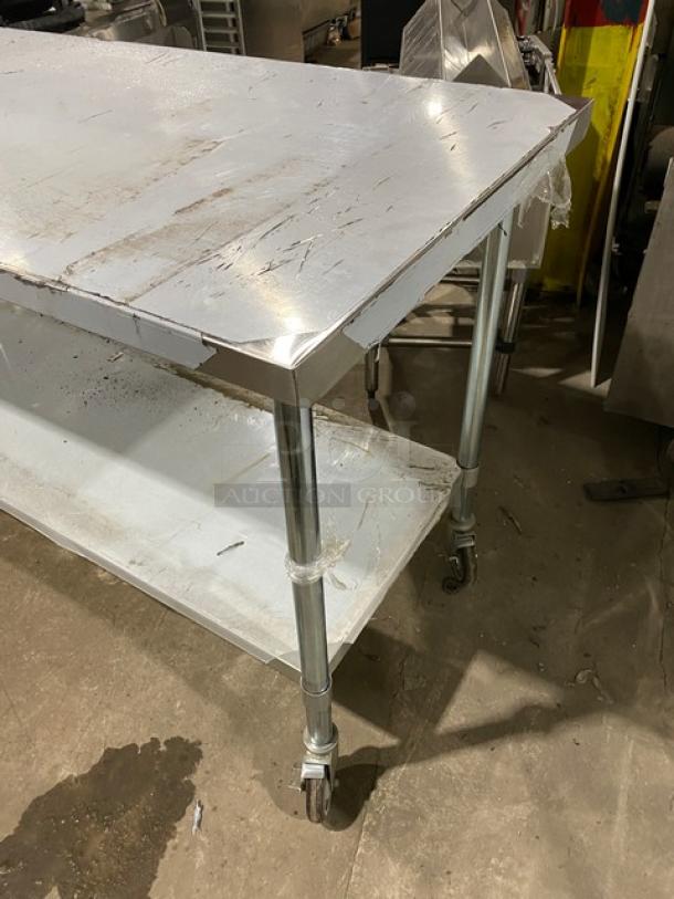 Commercial stainless steel worktop equipment table with undershelf, on casters, shows signs of wear, sturdy construction.