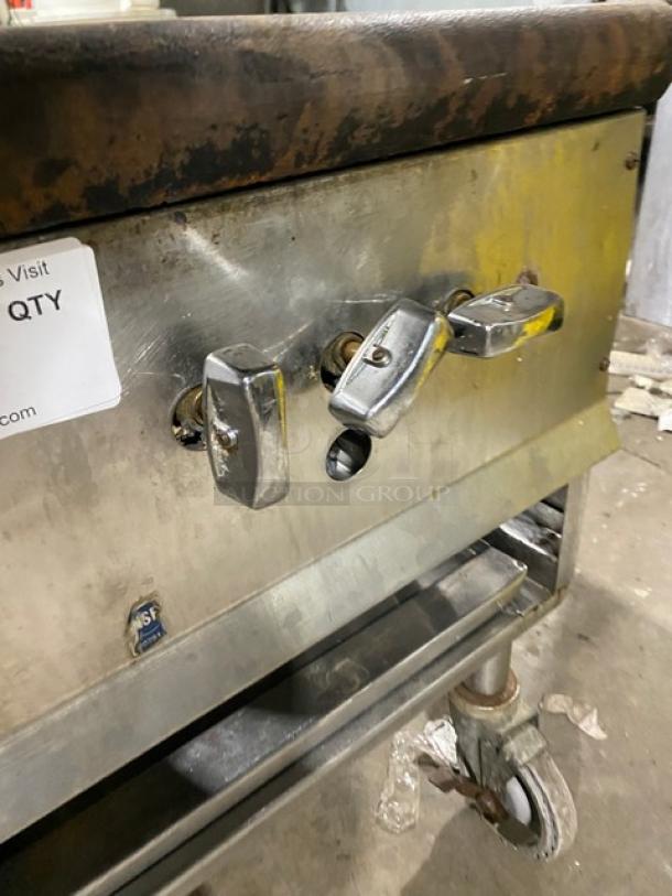 Commercial stainless steel gas-powered single burner stock pot range on casters, controls visible, used condition.