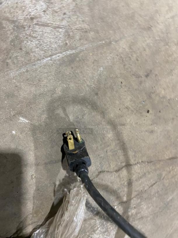 Plug of True TD2407 bottle cooler, 115V, 1 phase; black cord on concrete floor.