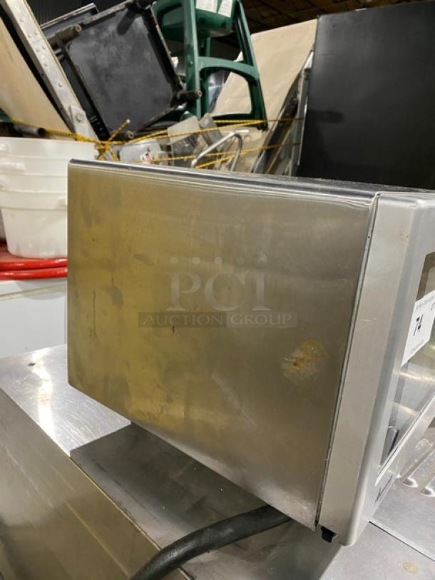 Amana RMS10DS stainless steel countertop microwave oven, electric-powered, visible wear on exterior, model and serial numbers marked.