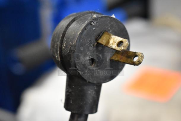 Close-up of a worn, black electrical plug with three prongs, showing signs of use and slight wear.