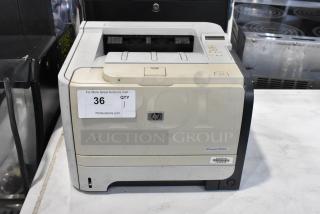 HP LaserJet P2055dn printer on countertop, used condition with visible wear. HP logo and model label present. Auction tag attached.