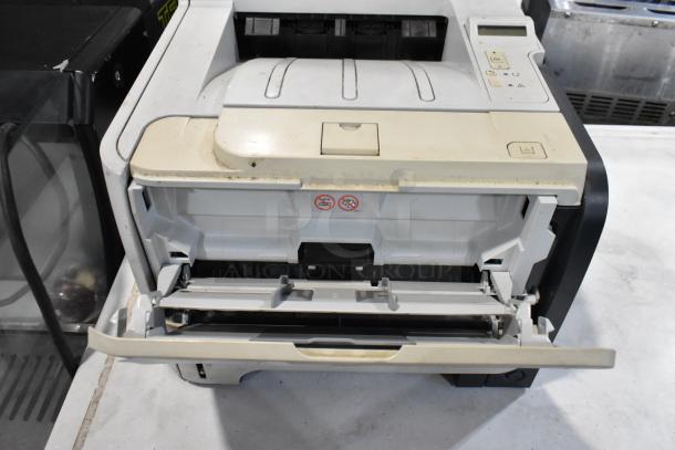 HP LaserJet P2055dn printer with open tray, shows signs of use, visible control panel and no visible damage.