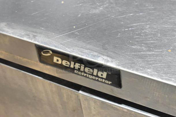 Delfield stainless steel commercial prep table with 4 drawers. Visible Delfield branding. Condition shows signs of use.