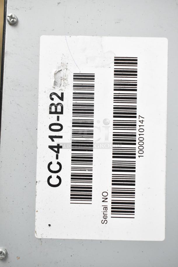Barcode label on a metal surface with text "CC-410-B2" and serial number "1000010147." Slight wear is visible.