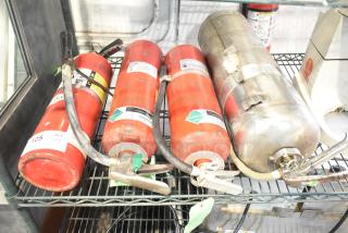 Four assorted fire extinguishers on a shelf; red and silver casings, visible labels, no shipping available, pickup required.