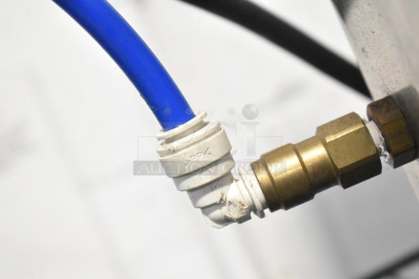 Close-up of a blue and brass connector part, possibly from the Bunn CDBCFP20 coffee machine. The connector is attached to a metal fitting, showing slight wear.