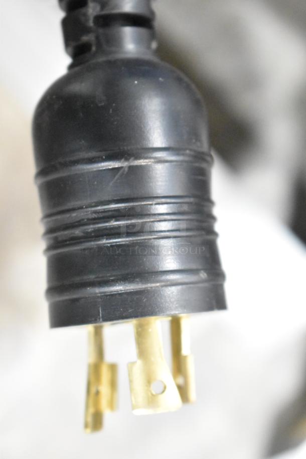 Close-up of a black and gold three-prong industrial plug with visible wear, likely part of a Jahabow merchandise display case.