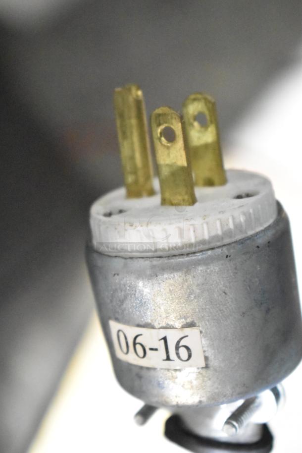 Close-up of a metal electrical plug for a claw machine game, labeled "06-16," featuring three brass prongs.