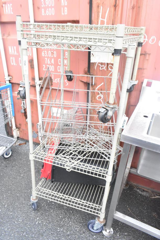 Tan 3-tier wire shelving unit with two extra shelves and commercial casters. Tags show marked numbers. Buyer to dismantle.