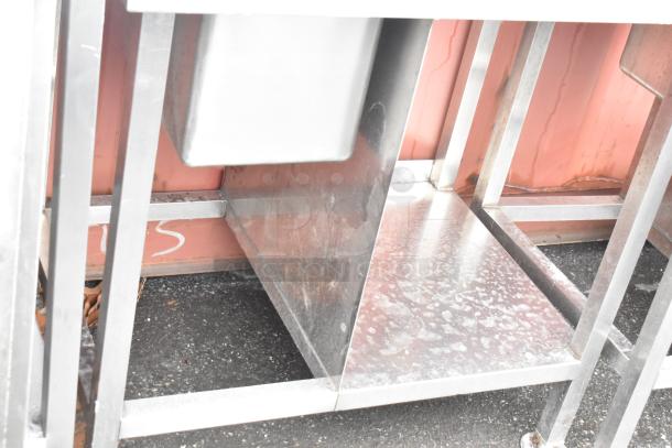 Stainless steel commercial single bay sink with backsplash and undershelf, good condition, visible wear on surfaces.