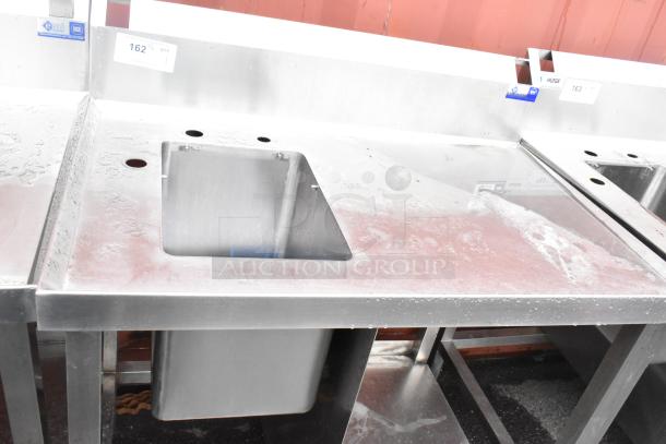Stainless steel commercial single bay sink with backsplash and under shelf, visible signs of wear, brand "EMI," model NSF.